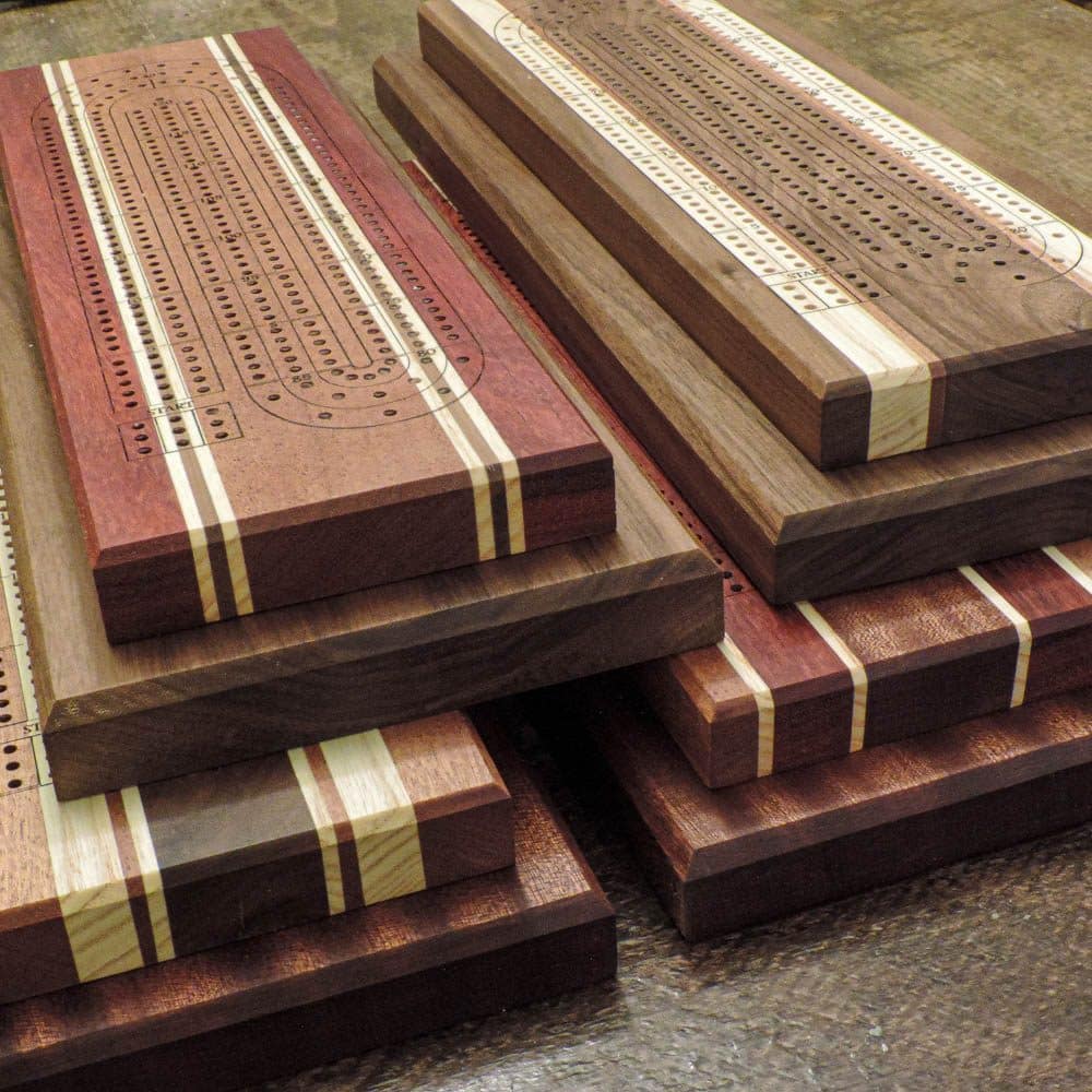 Wooden 2-tier cribbage boards, measuring 4 inches by 14 inches for the peg board and 6 inches by 15.25 inches for the base. The board is handcrafted from a mix of hardwoods such as Walnut, Maple, Cherry, Padauk, and Sapele.